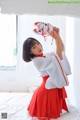 A woman in a red and white kimono holding a cat mask.