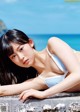 A woman in a white bikini laying on a rock by the ocean.