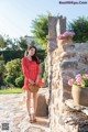 A woman in a red polka dot dress standing next to a stone wall.