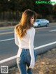 A woman in a white sweater and jeans standing on the side of the road.