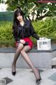 A woman in a black shirt and red skirt sitting on a bench.