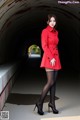 A woman in a red coat is standing in a tunnel.