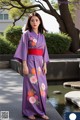 A woman in a purple kimono standing next to a pond.