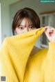 A woman in a yellow sweater covering her face with her hands.