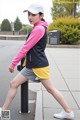 A woman in a pink hoodie and yellow shorts is walking down the street.