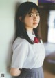 A young woman in a school uniform leaning against a wall.