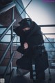 A woman in a black coat crouching down on a stairway.