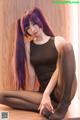 A woman with long purple hair sitting on a wooden floor.