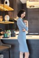 A woman in a blue dress standing in a kitchen.